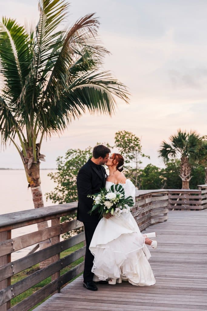 Bride and Groom kissing on a wooden bridge near the water, under a palm tree, Central FL