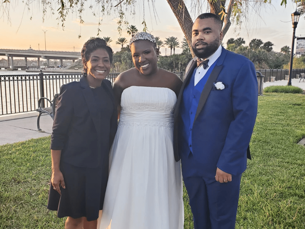 Couple with their celebrant outdoors on the lawn, bride in her white strapless dress, groom in a blue suit, celebrant in a black dress, Central FL