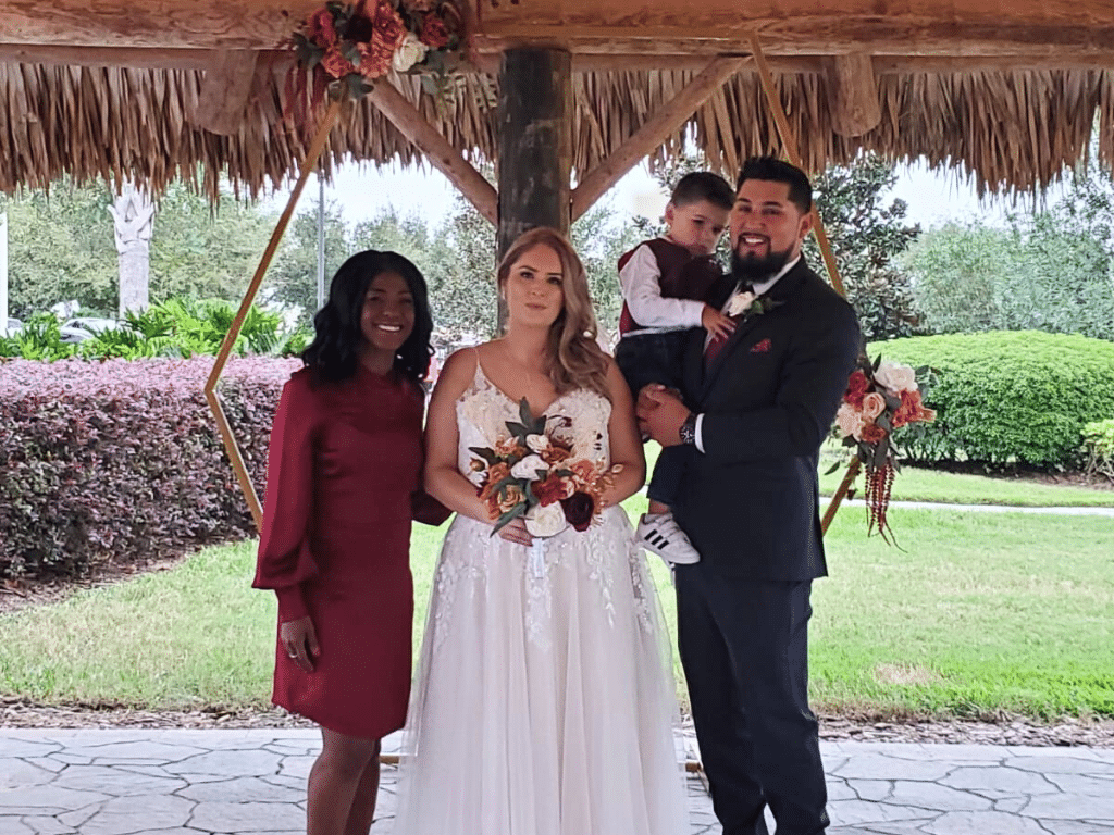 Wedding couple, groom holding their son, bride holding her bouquet, officiant wearing a maroon dress, Central FL