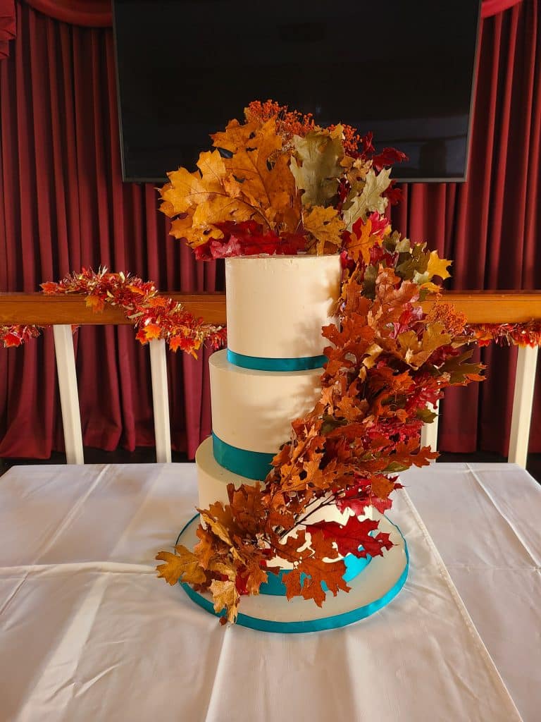 three layer cake with white fondant and blue ribbons around each layer, fall colored leaves wrapped around the layers of cake, Orlando, FL