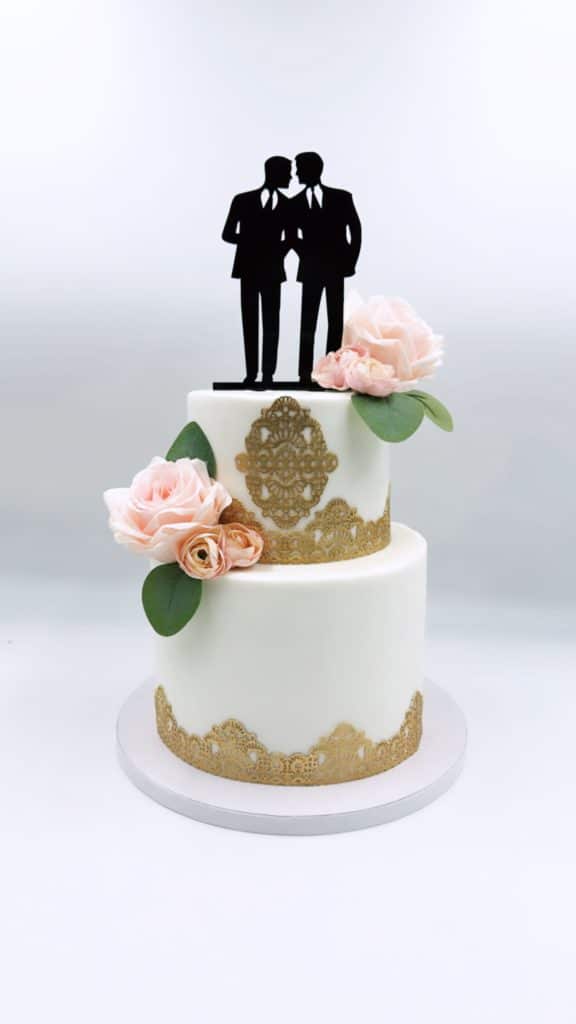 simple two tiered cake with gold adornments, one pink flower on each layer and a cake topper of two grooms in all black, Bells Cake House, Central FL