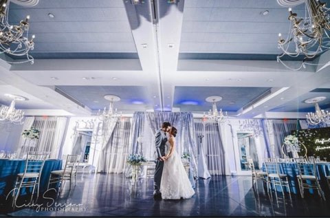 zoomed out photo of the ballroom, with blue tablecloths, white sheet curtains, silver chairs and few chandeliers hanging from the ceiling, LaBellaRose Ballroom, Central FL