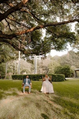 Bride and groom sitting on tree swings beneath a large oak tree at Club Lake wedding venue in Apopka Florida, surrounded by lush green woodland grounds