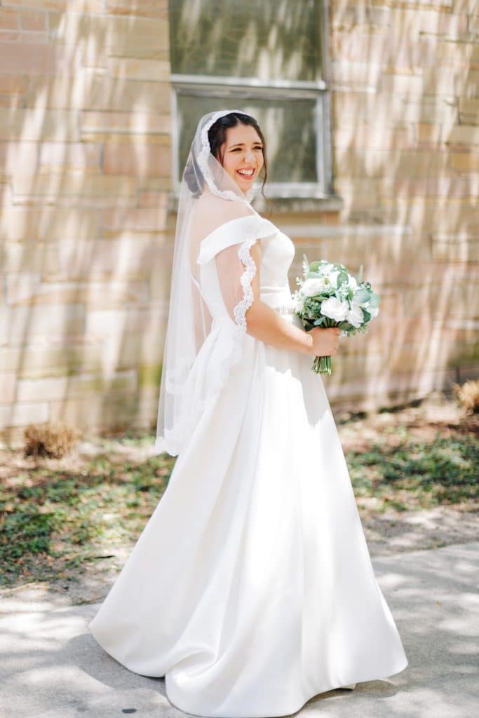 Bride in her wedding dress, with a sheer veil on her head, flowing down her back, white flower bouquet, outdoors, on a sidewalk, Alicia Frost Photography, Central FL