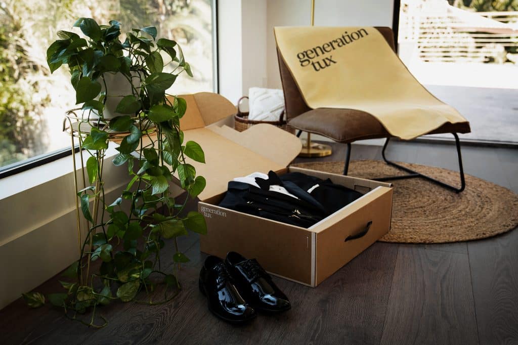 Flatlay of a tuxedo, shoes, garment bag on a chair near a plant by the window, Generation Tux