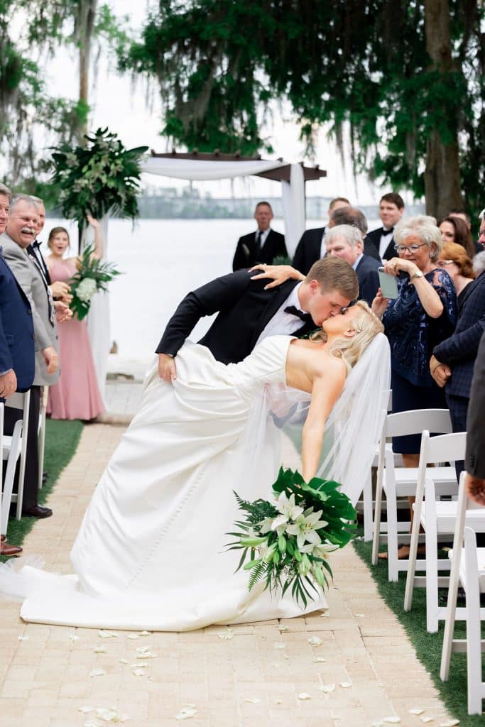Groom dipping his bride in the middle of the aisle, outdoors, near the water, Central, FL