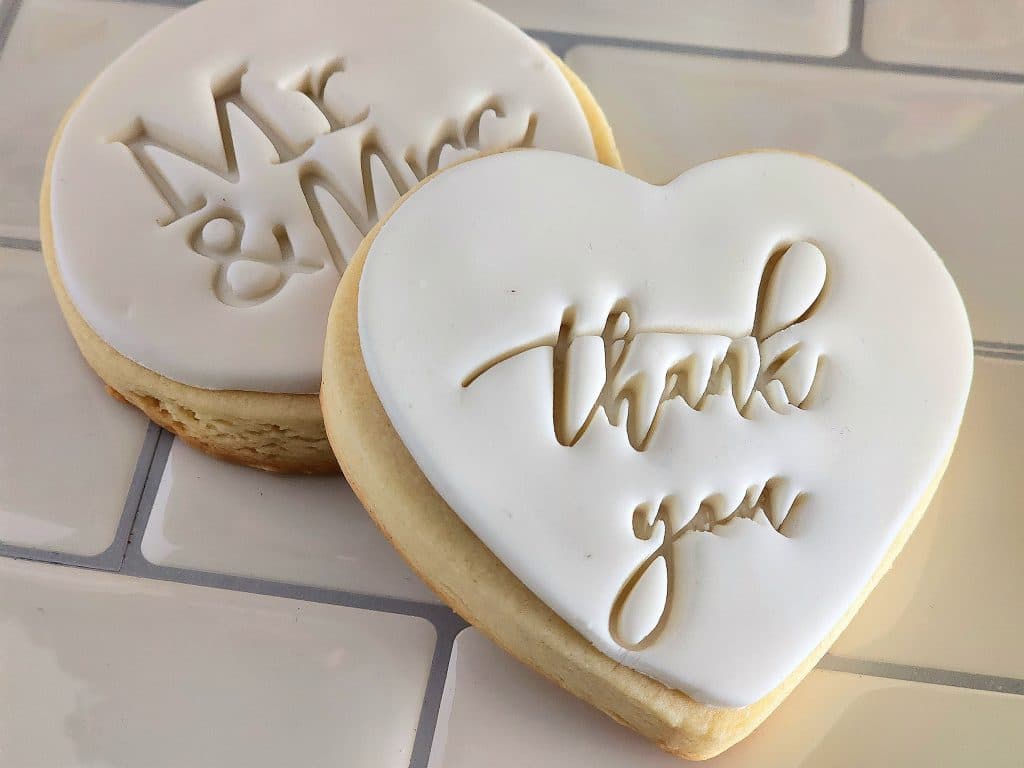 specialized cookies for a wedding, sitting on subway tile counter, one on the left is circle shaped, white icing, with Mr & Mrs on it, the right one is heart shaped, white icing and Thank You on it, Special Treats by Tanya, Orlando, FL