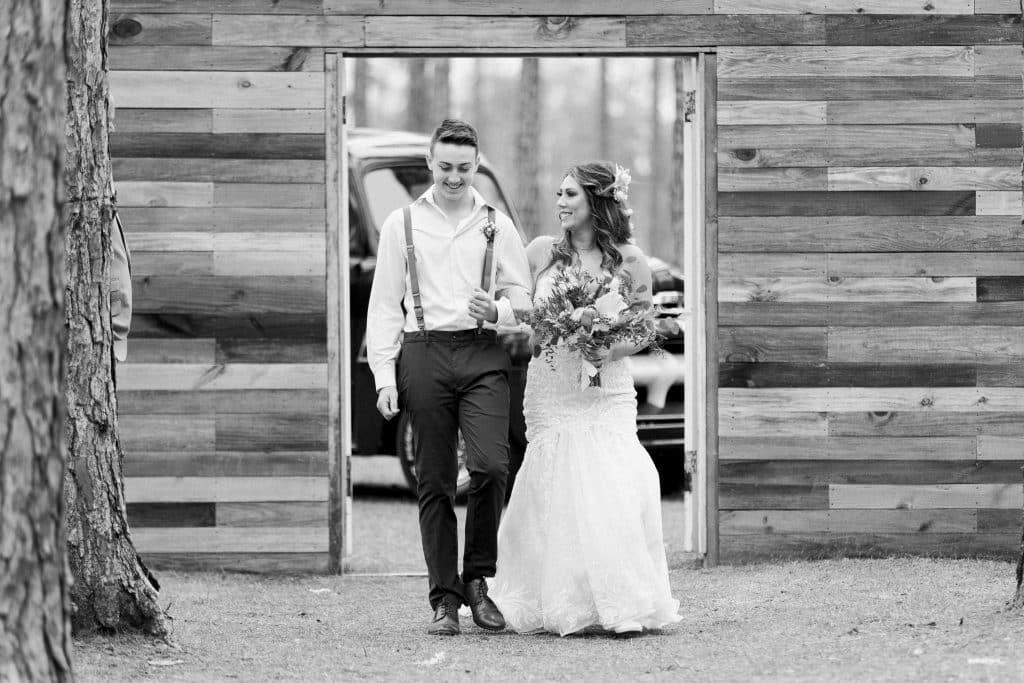 Black and white photo of bride and groom walking arm in arm, wooden wall backdrop, Alicia Frost Photography, Central FL