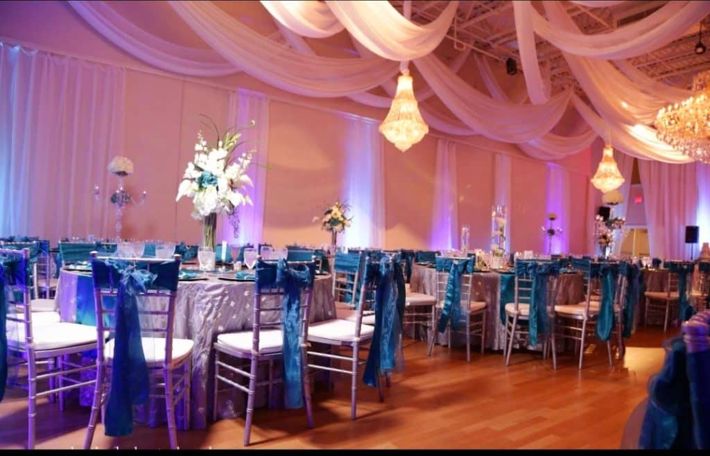Reception set up with tables and high back chairs, with teal chair covers for the backs, tall centerpieces with white flowers, purple uplighting throughout the room, JoJo's Glitz & Glam Event Planning, Central FL