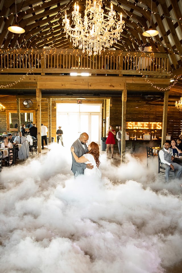 Bride and Groom on the dance floor at their reception in a barn, with smoke billowing into the area, with a chandelier above and guests looking on, Uptown Selfies, Central FL