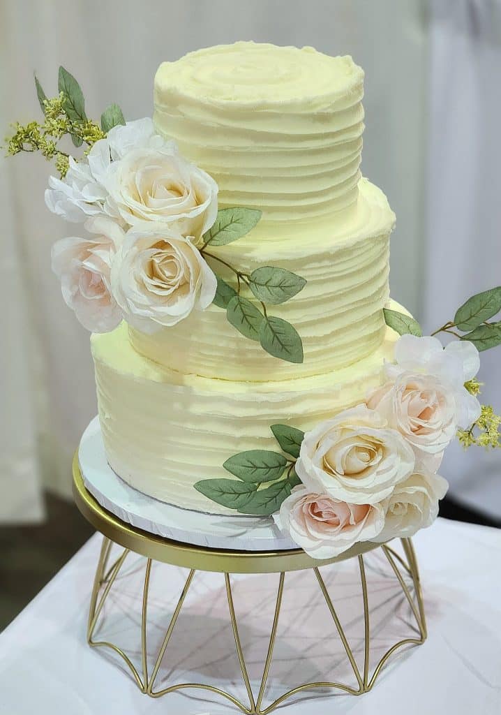 three layer cake with light yellow frosting, white and pink flowers on each layer, on a gold stand, Orlando, FL
