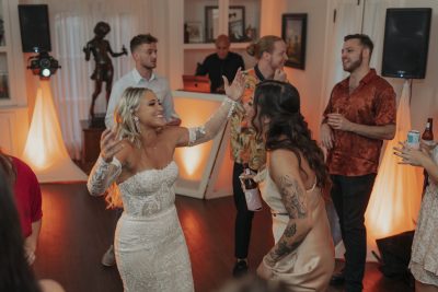DJ set up in the background, women dancing at a wedding in the foreground, orange uplighting, DJ Rey, Central FL