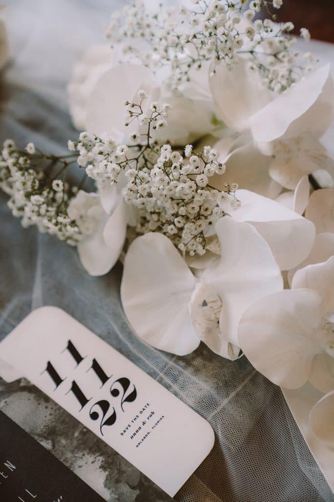 Flatlay of flower and invitations on white sheer materials on a dark table, Central FL