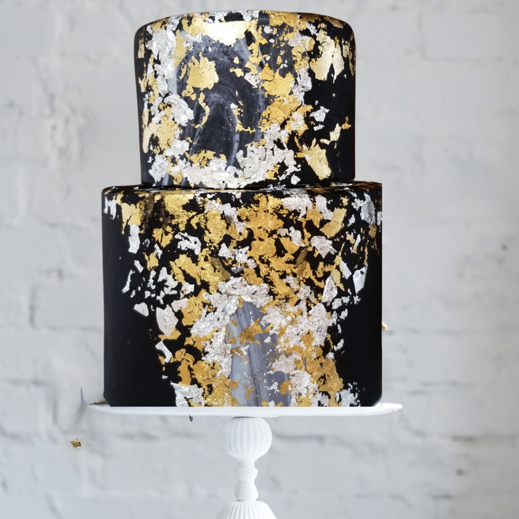 Two tiered cake with black fondant and a speckling of gold and white sitting on a white cake stand, Orlando, FL