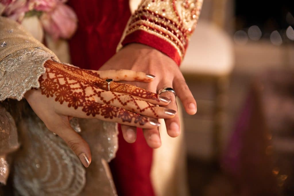 Close up of a Bride and Groom touching hands, bride has henna tattoos on her hand and wrist