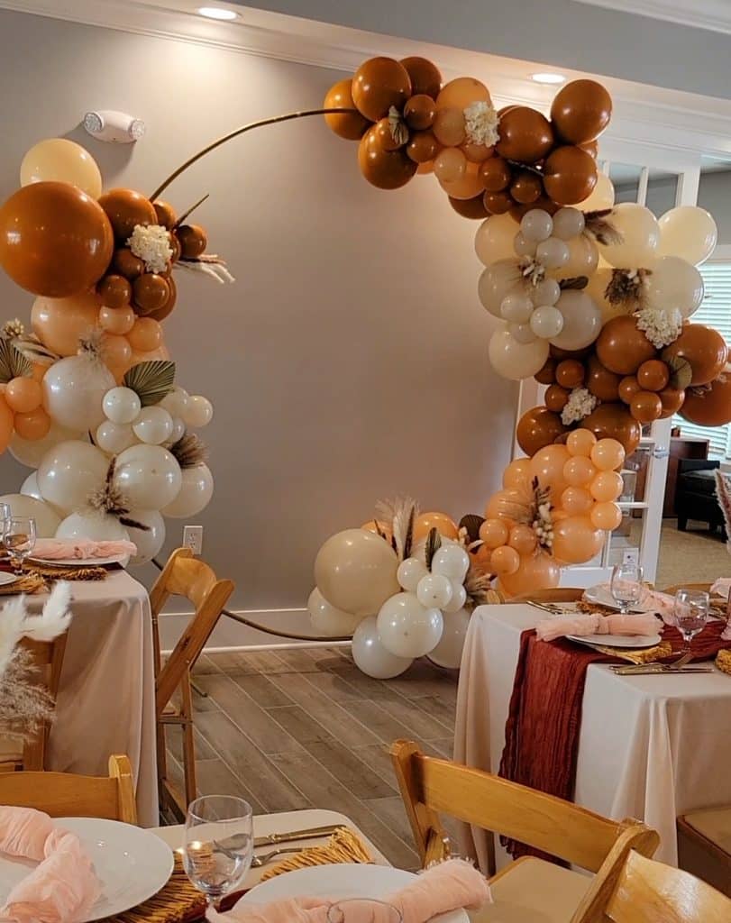 Building a fall color themed balloon arch with browns, whites, oranges in an event space with tan tablecloths on tables with brown runners, Central FL