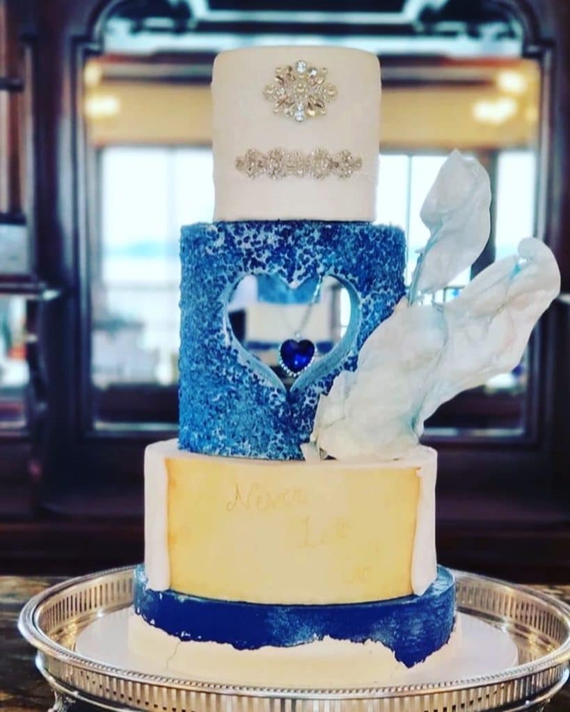 three tiered cake, top layer is white with silver adornments, middle layer is blue with a cut out heart, bottom layer is white with exposed cake on a silver platter, Bells Cake House, Central FL