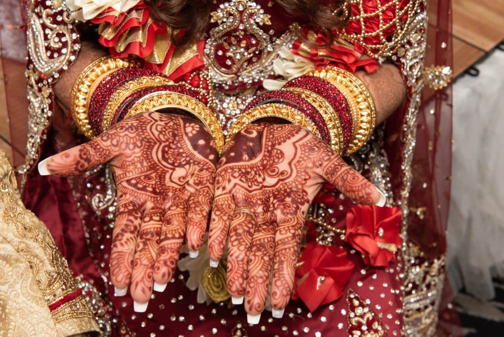 Woman showing off her henna tattoos that accompany her ornate attire and jewelry in red and gold, Central, FL