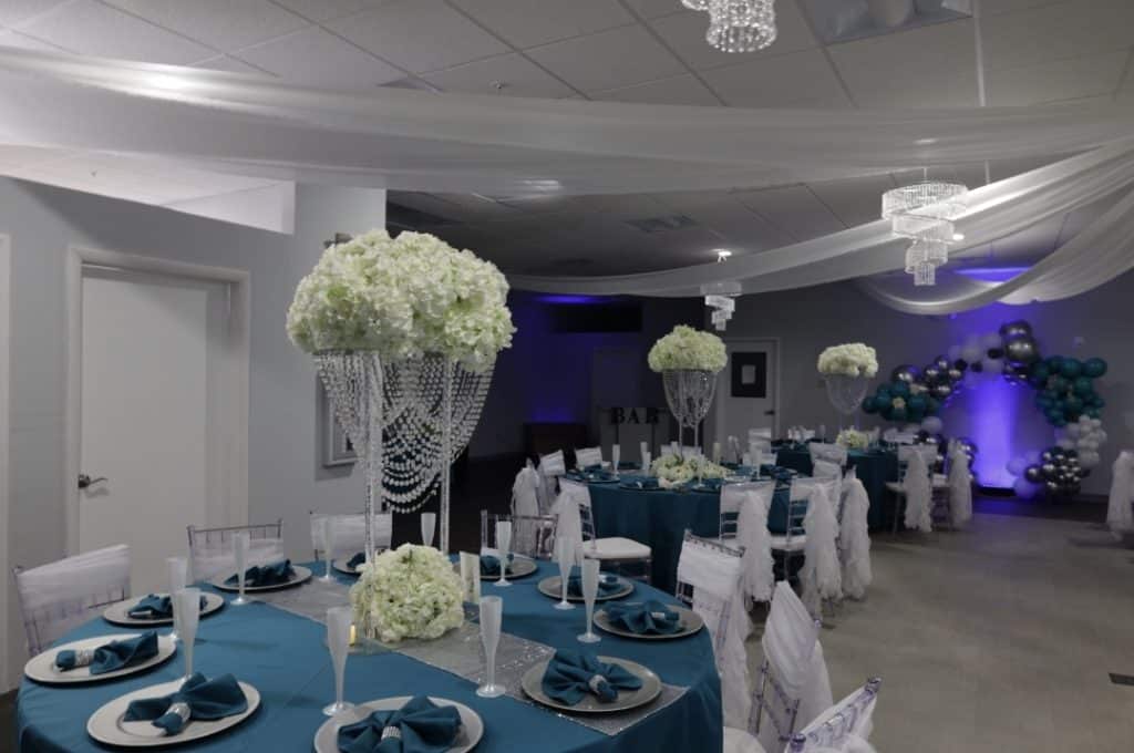 Special event set up with teal table settings, teal napkins and silver chargers, tall white centerpieces, sheer white chair back ribbons, purple uplighting, Central FL