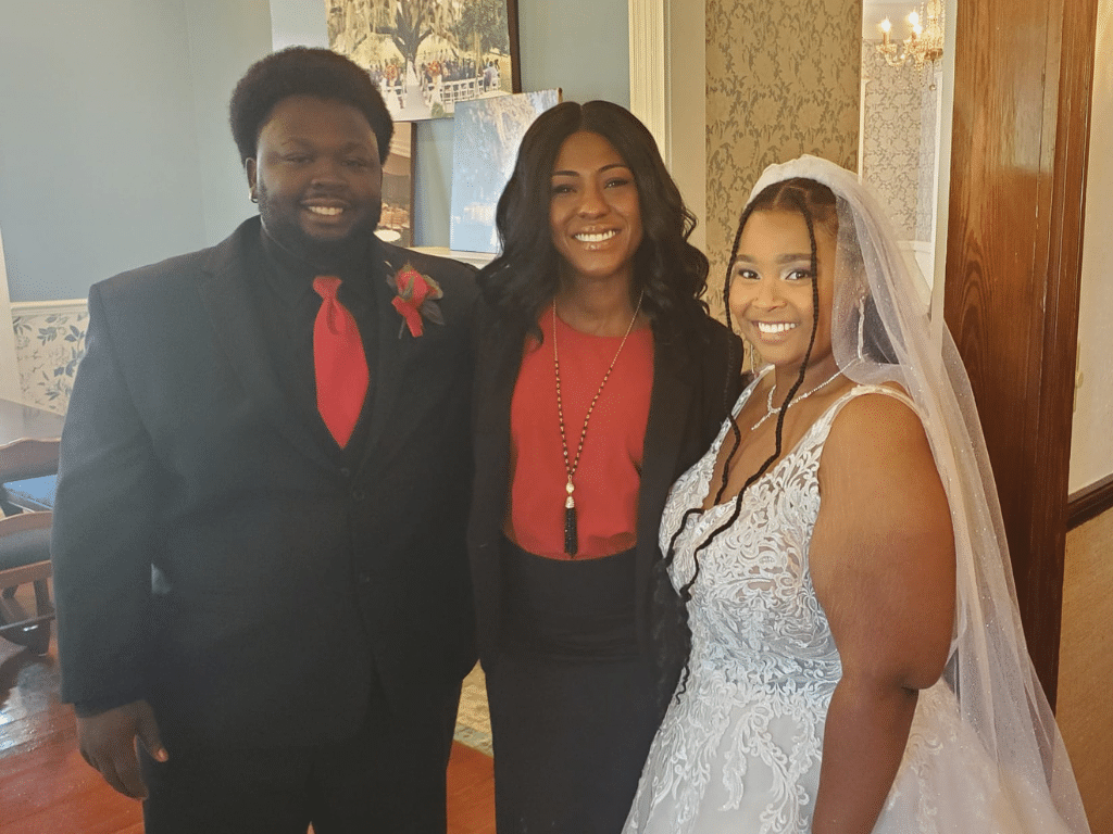 Officiant poses with her bride and groom, bride in her wedding dress, officiant and groom are wearing black with pops of red, Central FL