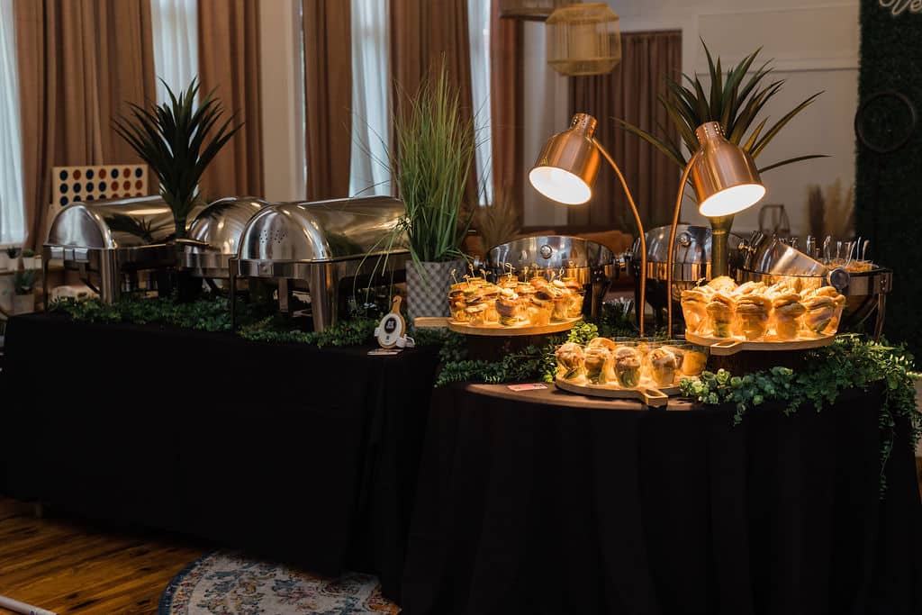 food station setup in room with black linen covered tables and two heat lamps on one end