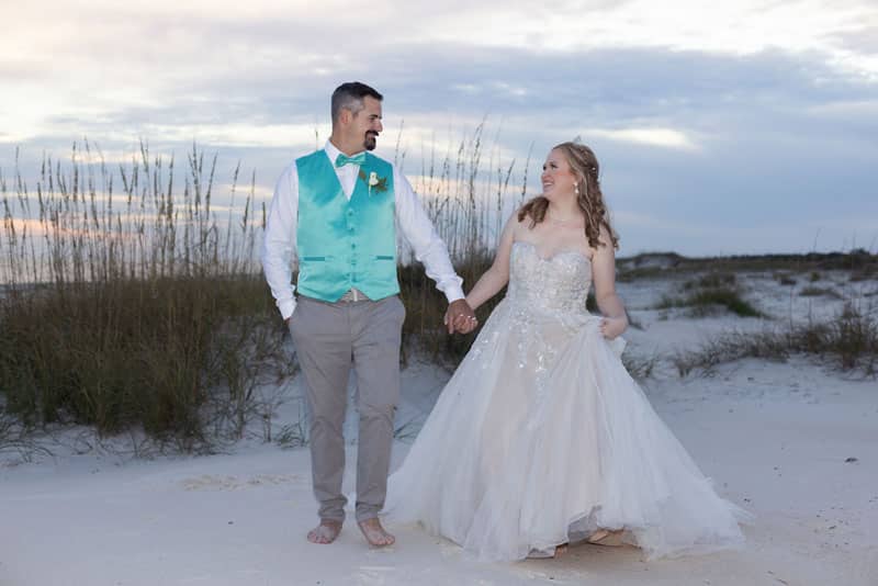 Married couple walking on the beach, near sunset, groom wearing a baby blue vest with grey suit pants, bride in a white princess style gown, central FL
