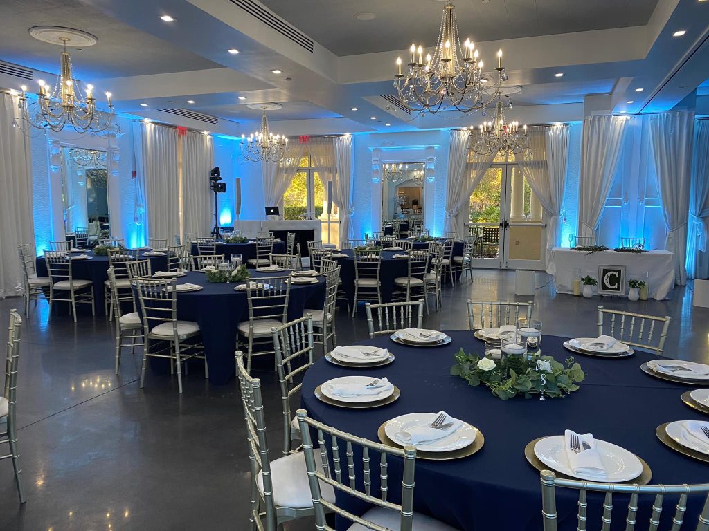 Ballroom set for special event with blue tablecloths, silver chargers, white plates and white napkins, silver chairs and blue uplighting around the room, LaBellaRose Ballroom, Central FL