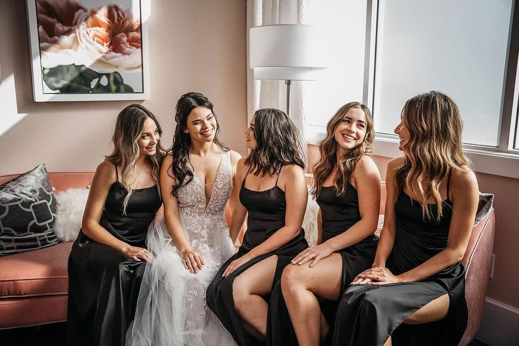 Bride with her wedding attendants, in black gowns, sitting on a mauve sofa, in a sitting room, Central FL