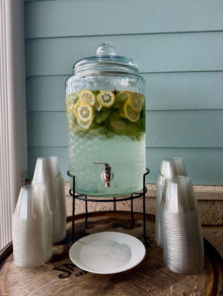 Lemon and cucumber water in a large glass serving container with plastic serving cups on a wooden serving tray, Central FL
