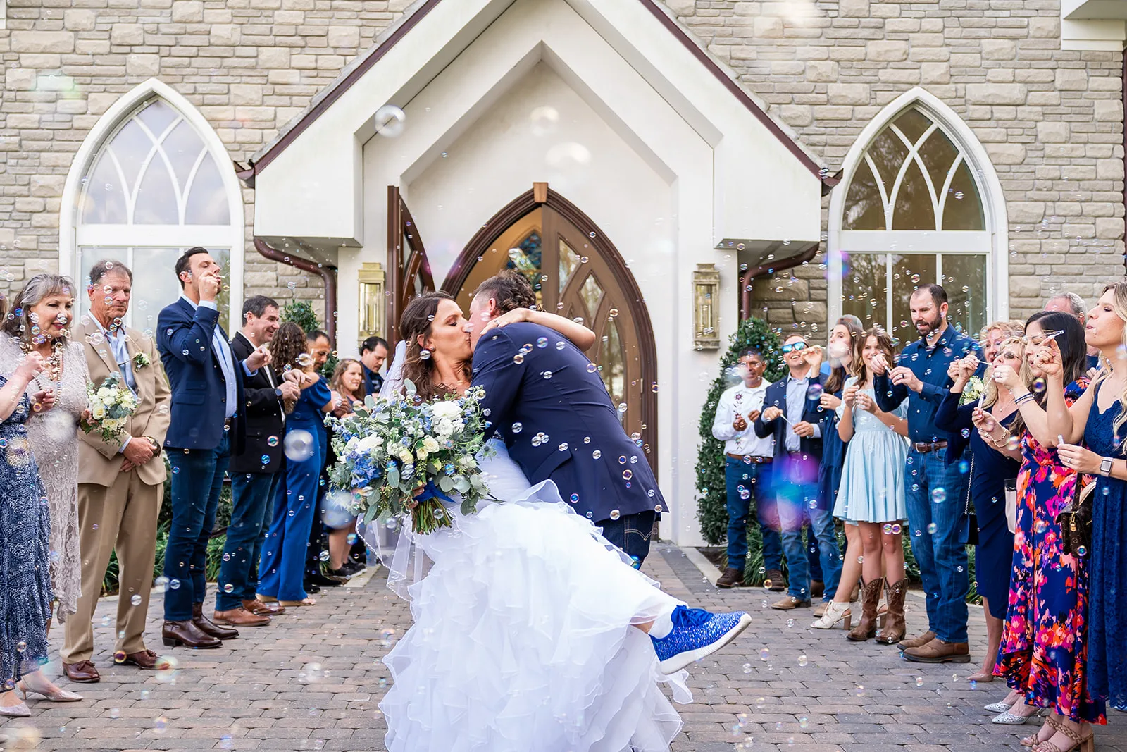 Bride and groom share a romantic dip kiss during a bubble send-off exit outside the chapel at World Equestrian Center in Ocala, Florida, surrounded by cheering wedding guests