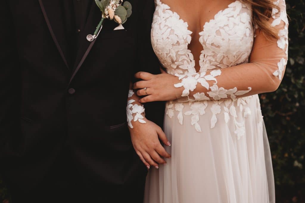 Photo of the wedding couple standing arm in arm, view is from the chest down to show the detailed lace on her dress, Central FL