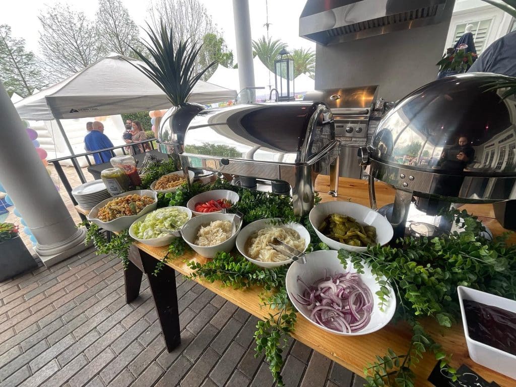 Catering setup with silver chaffing dishes, with large white bowls displaying the sides, all dressed with lemon leaves as decoration, outdoors, Creations Cuisine Inc, Central FL