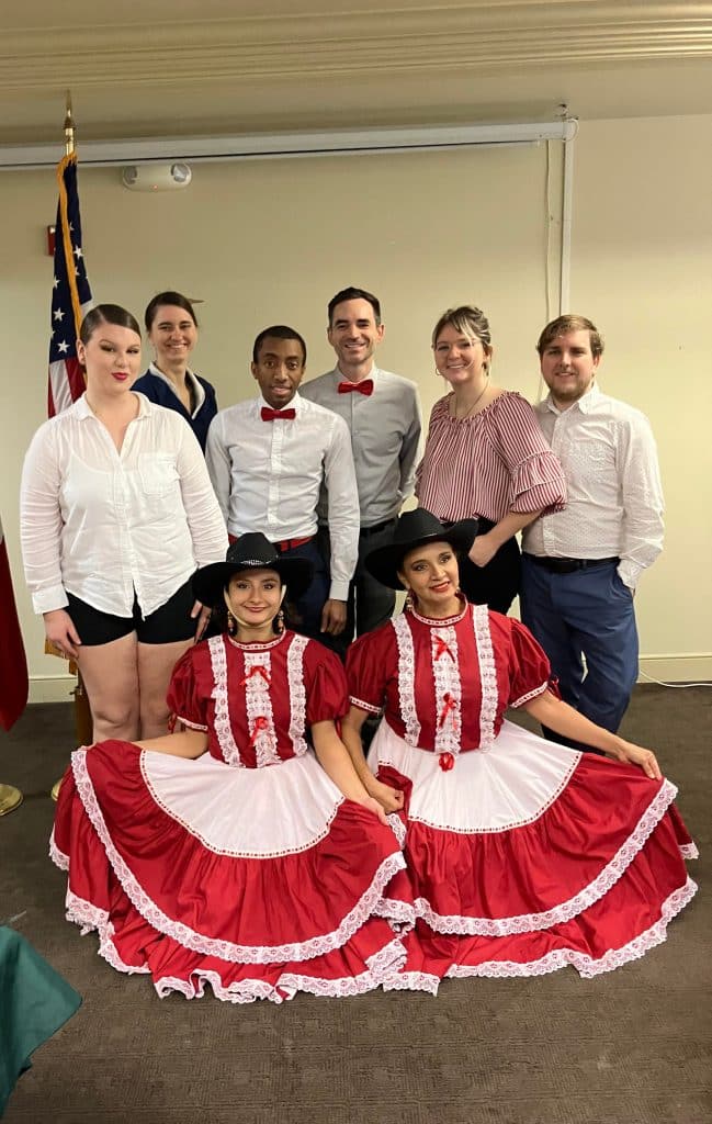 Dancers posing together, two women wearing red and white dresses as costumes, everyone else in dark bottoms and light tops, Vintage Dance Company, Central FL