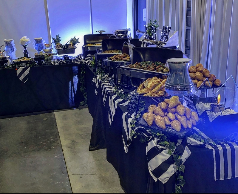 Queen Chef Catering, full display of catering with chaffing dishes on black tablecloths, blue uplighting, black and white striped overlays, Central FL