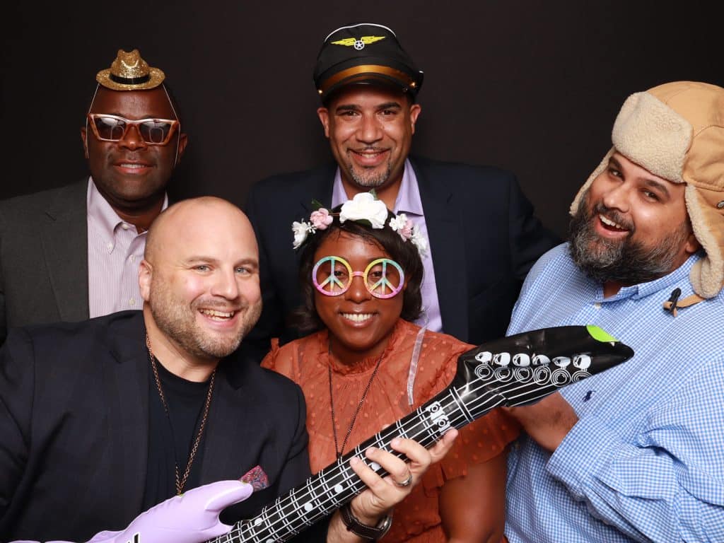 Guests wearing fun hats and holding an inflatable guitar for a group photo, The PhotoBooth Company, Central FL