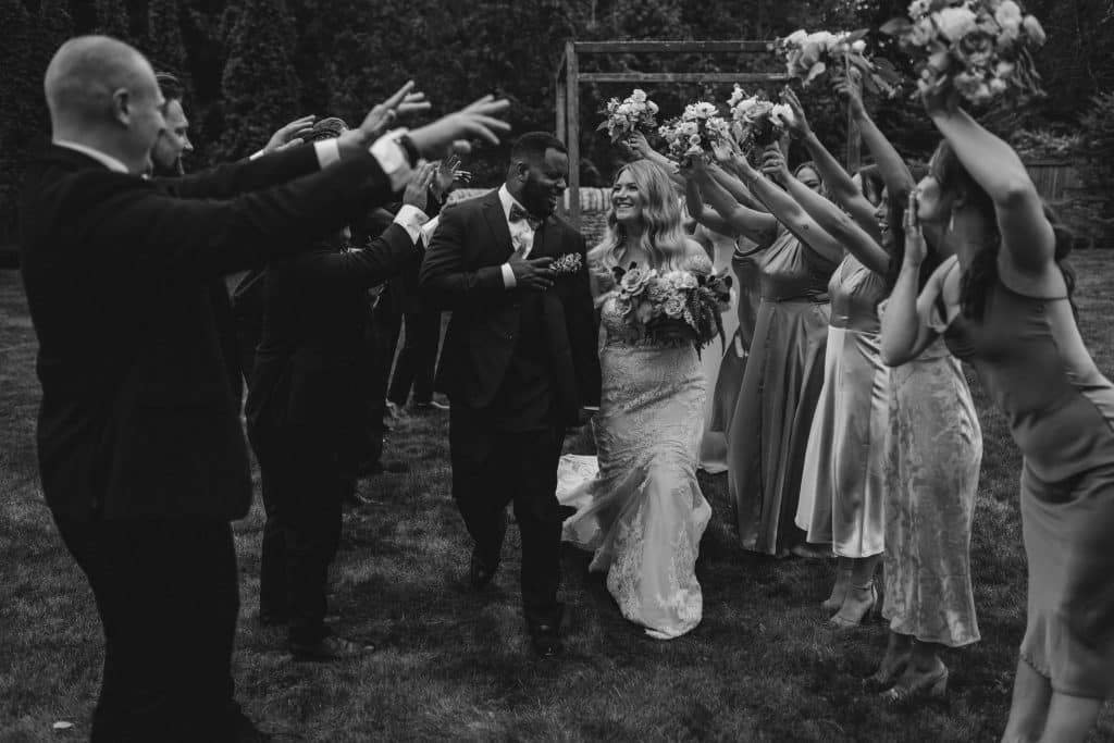 Black and White photo, Wedding party holding their arms up so the bride and groom can walk through their line, Ashley Krug Photography, Central FL