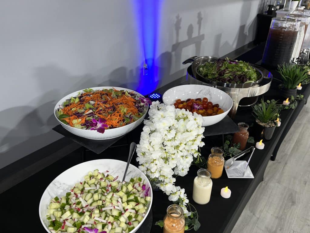 A variety of salads on display on a buffet station with dressings in front in small glass jars, Queen Chef Catering, Central FL