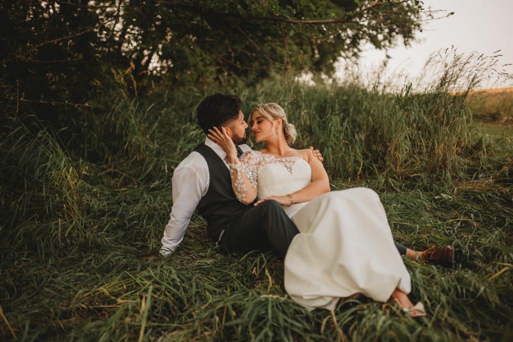Wedding couple lounging in the grass near trees, outdoors, bride in her white dress, groom in his black tuxedo, Ashley Krug Photography, Central FL
