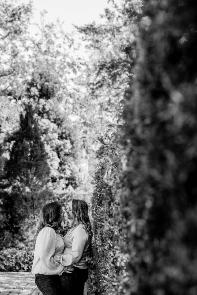 Two women stealing a private moment during their engagement photo shoot, outdoors, surrounded by trees and flowers, XOXO Sarai Photography, Central FL