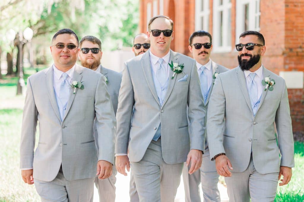 Groom and groomsmen wearing grey suits with white shirts and light blue ties and wearing black sunglasses all walking towards the camera, XOXO Sarai Photography, Central FL