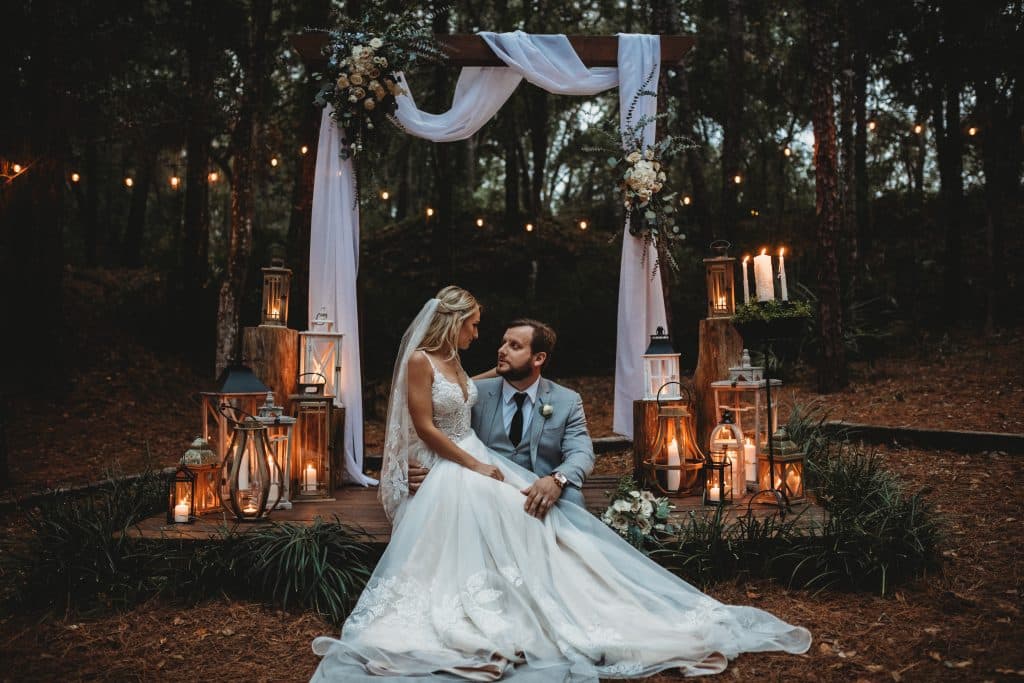 Wedding couple, post ceremony, sitting on the wooden stage where their ceremony took place, at night, with lanterns and candles lighting the area, Ashley Krug Photography, Central FL