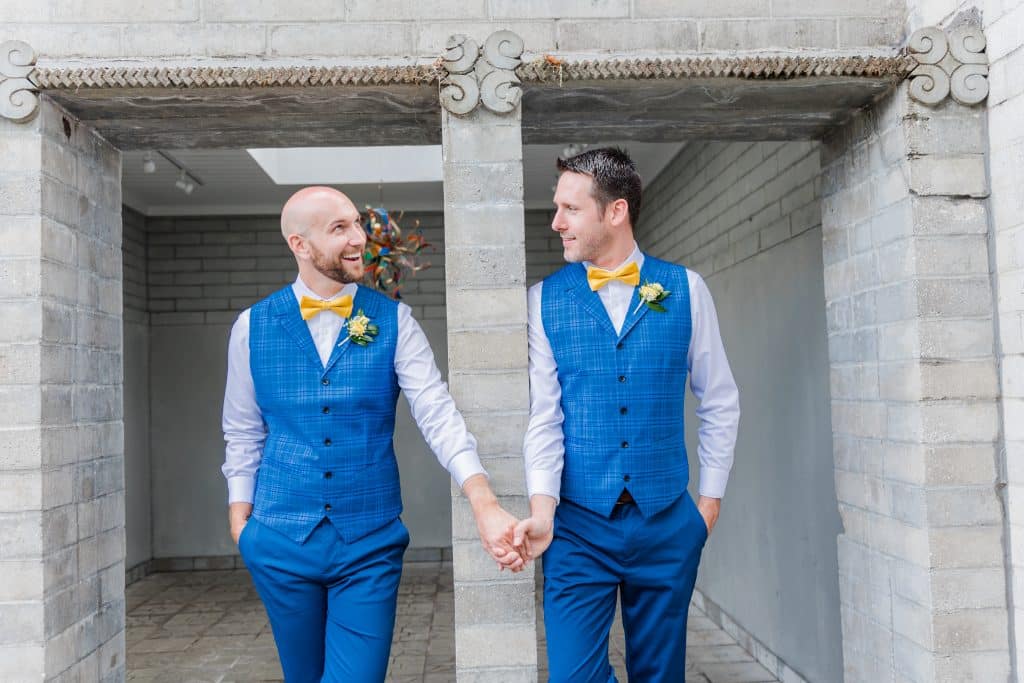 Couple wearing matching blue suits, holding hands outdoors in an square archway, Central FL