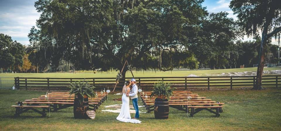 zoomed out shot of the couple on the ranch, in front of the ceremony benches, Peacock Ranch Wedding Venue, Orlando, FL