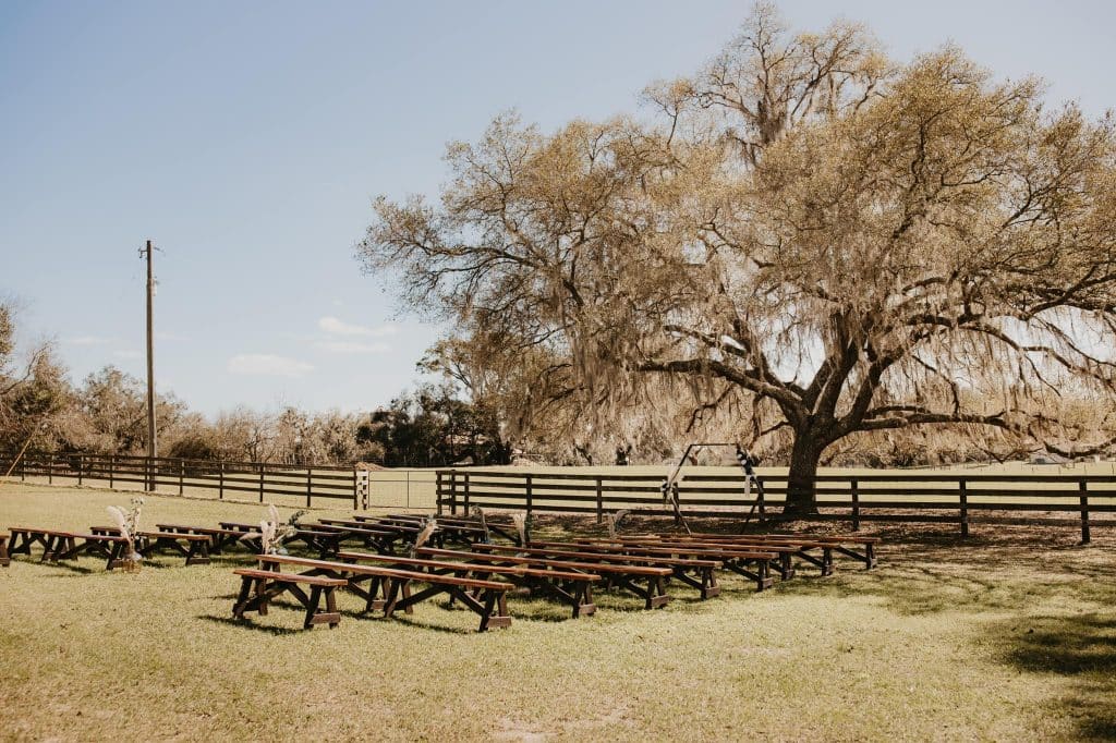 Peacock Ranch Wedding Venue, benches set out for a ceremony, under a large tree, with a fence behind, Orlando, FL