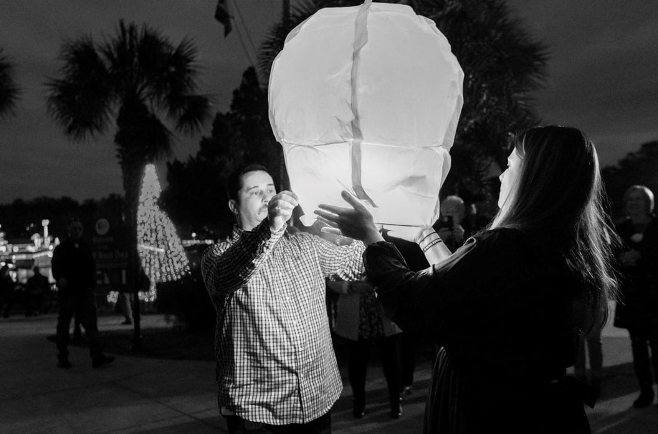 black and white image of couple holding a floating white lantern they're about to release at night time