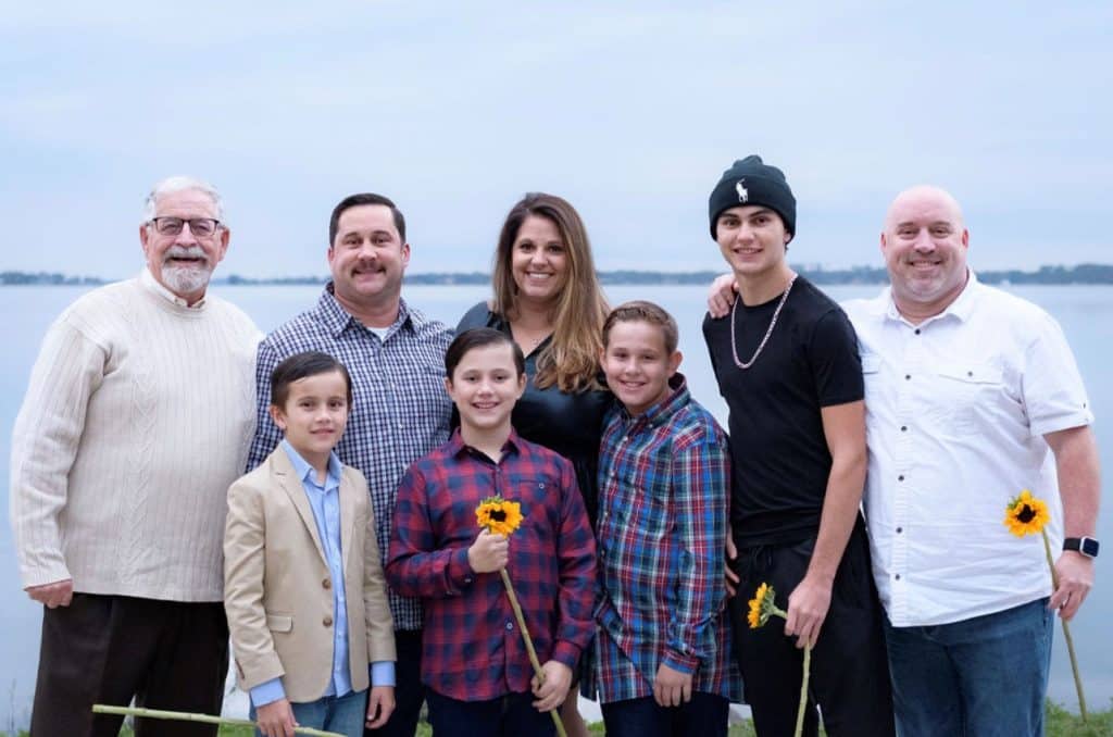 family poses together smiling for picture in front of body of water