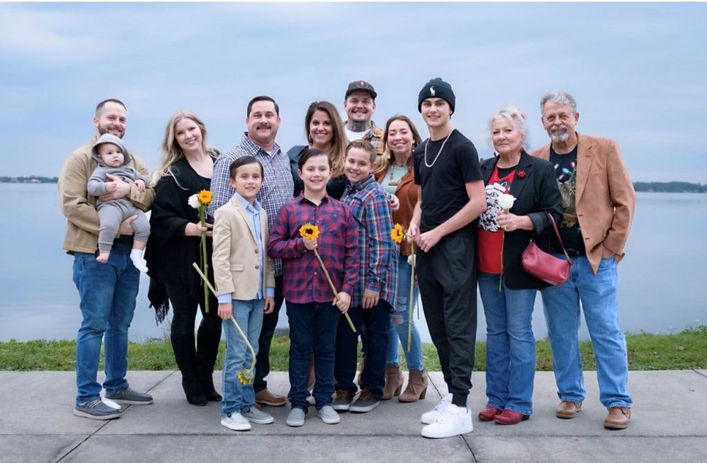 family poses together smiling for picture in front of body of water