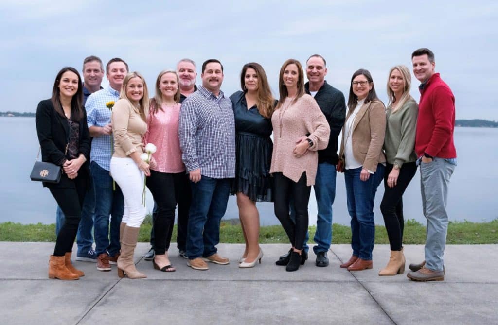 family poses together smiling for picture in front of body of water