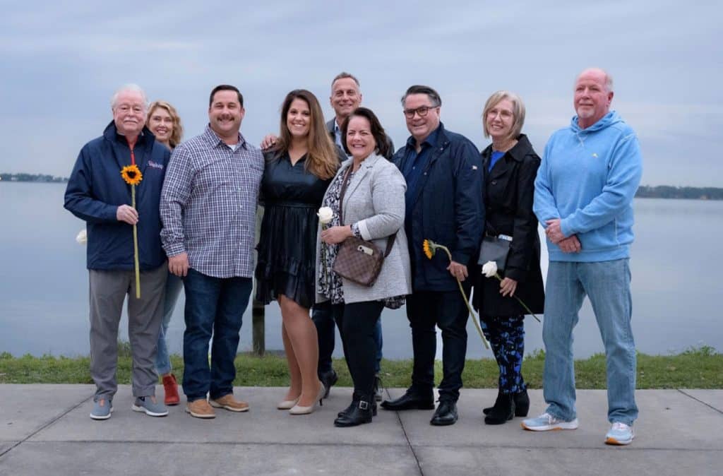 family poses together smiling for picture in front of body of water
