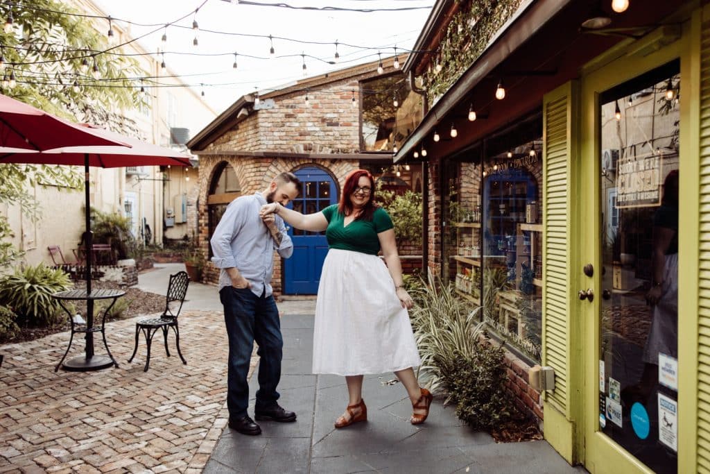 man leans over holding womans hand kissing it while woman looks down and hold white skirt out